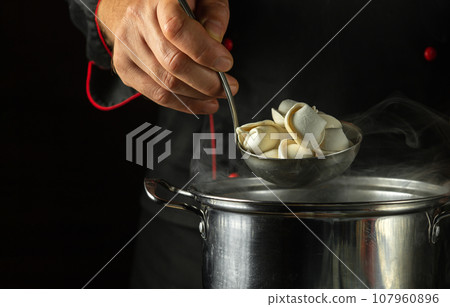 The chef prepares pelmeni or dumplings in a saucepan in the restaurant kitchen. Close-up of a cook hand while working 107960896