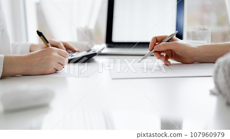 Two accountants using a laptop computer and calculator for counting taxes at white desk in office. Teamwork in business audit and finance 107960979