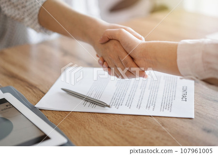 Business people shaking hands above contract papers just signed on the wooden table, close up. Lawyers at meeting. Teamwork, partnership, success concept 107961005