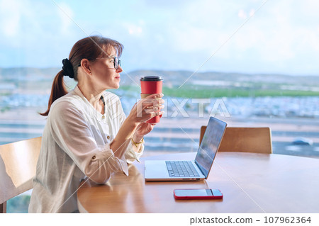 Middle aged woman in airport cafe working with laptop computer 107962364