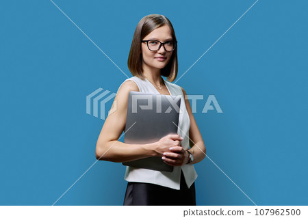 Young confident woman with laptop computer in hands on blue background Young confident woman with laptop computer in hands on blue background 107962500