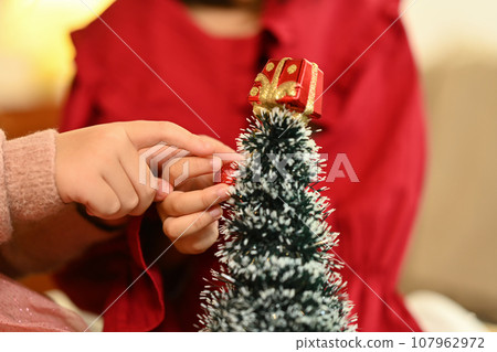 Two little children hands decorating small Christmas tree in living room 107962972
