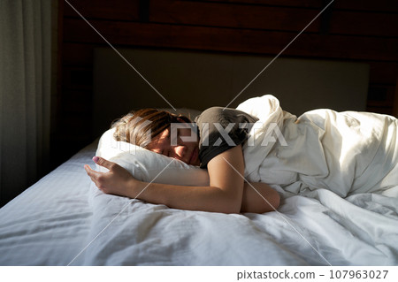 Female is sleeping cozily on a bed at the bedroom. Female is sleeping cozily on a bed at the bedroom. 107963027