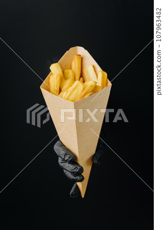 Hand holding French fries through torn holes in black paper background. Street food concept 107963482