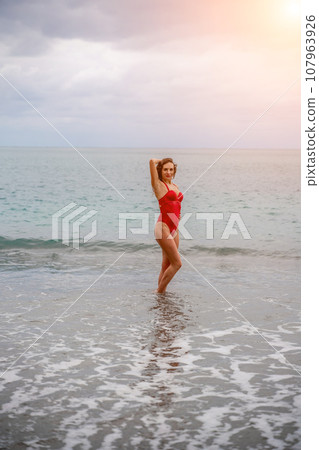 A beautiful and sexy brunette in a red swimsuit on a pebble beac A beautiful and sexy brunette in a red swimsuit on a pebble beac 107963926