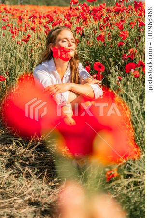 Woman poppies field. Happy woman is resting in the rays of the sun sitting in the poppy field. Woman poppies field. Happy woman is resting in the rays of the sun sitting in the poppy field. 107963968