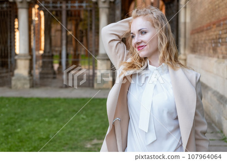 Portrait of attractive red-haired girl in spring outdoors. Cute blonde girl in white blouse and coat outside smiling and looking at the camera 107964064