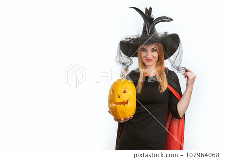 Dissatisfied young woman in witch hat with jack-o-lantern in her hands. Black clothes. Halloween party. White background, space for text Dissatisfied young woman in witch hat with jack-o-lantern in her hands. Black clothes. Halloween party. White background, space for text 107964068