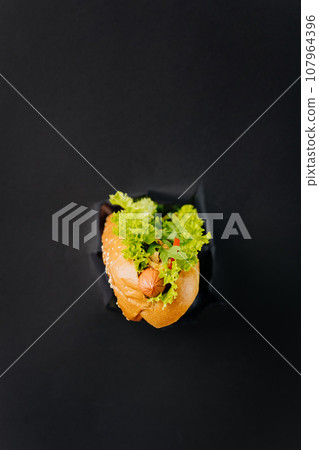 Fresh tasty hot dog sticks out through torn holes in paper background. Street food concept Fresh tasty hot dog sticks out through torn holes in paper background. Street food concept 107964396