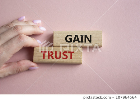 Gain trust symbol. Wooden blocks with words Gain trust. Beautiful pink background. Businessman hand. Business and Gain trust concept. Copy space. Gain trust symbol. Wooden blocks with words Gain trust. Beautiful pink background. Businessman hand. Business and Gain trust concept. Copy space. 107964564