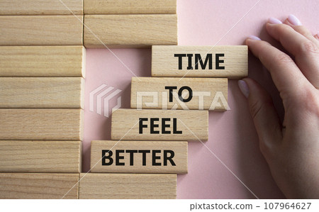 Time to feel better symbol. Wooden blocks with words Time to feel better. Businessman hand. Beautiful pink background. Medicine and Time to feel better concept. Copy space. Time to feel better symbol. Wooden blocks with words Time to feel better. Businessman hand. Beautiful pink background. Medicine and Time to feel better concept. Copy space. 107964627