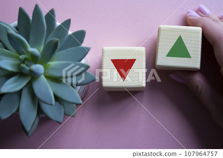 Interest rate symbol. Businessman hand is making a choice between two cubes with arrow going down and arrow going up. Beautiful pink background with succulent plant. Business concept. Copy space. 107964757