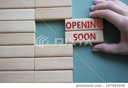 Opening soon symbol. Concept word Opening soon on wooden blocks. Businessman hand. Beautiful grey green background. Business and Opening soon concept. Copy space Opening soon symbol. Concept word Opening soon on wooden blocks. Businessman hand. Beautiful grey green background. Business and Opening soon concept. Copy space 107964840