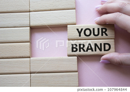 Your Brand symbol. Concept word Your Brand on wooden blocks. Businessman hand. Beautiful pink background. Business and Your Brand concept. Copy space Your Brand symbol. Concept word Your Brand on wooden blocks. Businessman hand. Beautiful pink background. Business and Your Brand concept. Copy space 107964844