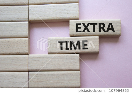 Extra time symbol. Concept word Extra time on wooden blocks. Beautiful pink background. Business and Extra time concept. Copy space 107964863
