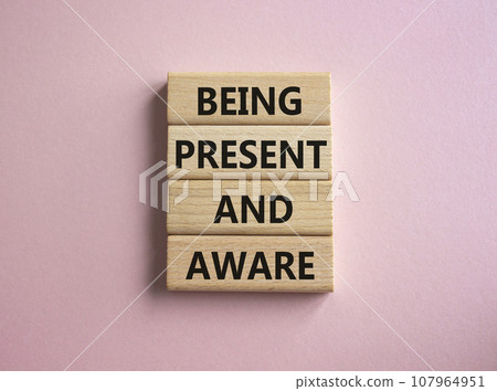 Being Present and Aware symbol. Wooden blocks with words Being Present and Aware. Doctor hand. Beautiful pink background. Psychology and Being Present and Aware concept. Copy space. 107964951