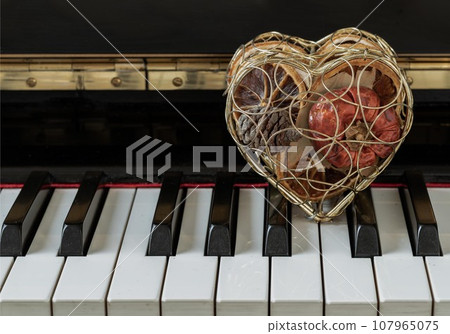 Golden heart shaped mesh case is filled with dried fruits stand on the Piano Keyboard. Golden heart shaped mesh case is filled with dried fruits stand on the Piano Keyboard. 107965075
