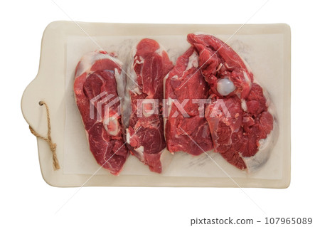Lamb meat on a ceramic board isolated on white background. Pieces of meat for cooking. Rear part of the meat carcass. Top view. Lamb meat on a ceramic board isolated on white background. Pieces of meat for cooking. Rear part of the meat carcass. Top view. 107965089