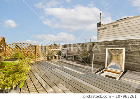 a wooden deck with chairs and plants in the fore - windowed area on the left side of the photo a wooden deck with chairs and plants in the fore - windowed area on the left side of the photo 107965261
