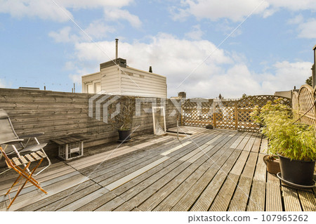 a wooden deck with chairs and potted plants in the foreground, against a blue sky filled with white clouds a wooden deck with chairs and potted plants in the foreground, against a blue sky filled with white clouds 107965262