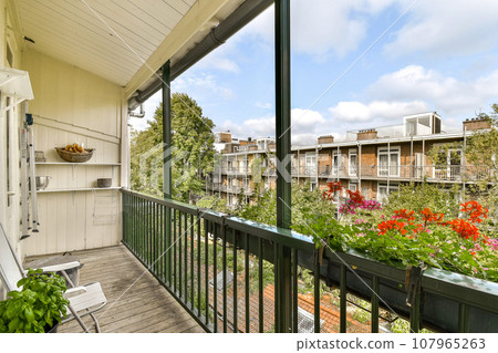 a balcony with flowers and plants on the railings, as seen from an apartment window looking out onto the street 107965263