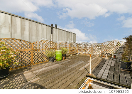 a wooden deck with pots and plants on the side, against a cloudy blue sky in the back ground a wooden deck with pots and plants on the side, against a cloudy blue sky in the back ground 107965265