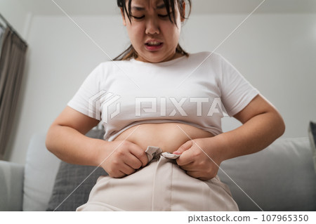 Fat chubby woman trying to wear tight pants, overweight, weight gain, Healthy and medical concept. 107965350