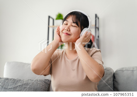 Young woman listening to music with headphone and relaxing while sitting on the sofa at home. 107965351