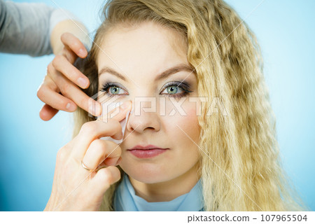Woman using oil blotting tissues on model Woman using oil blotting tissues on model 107965504