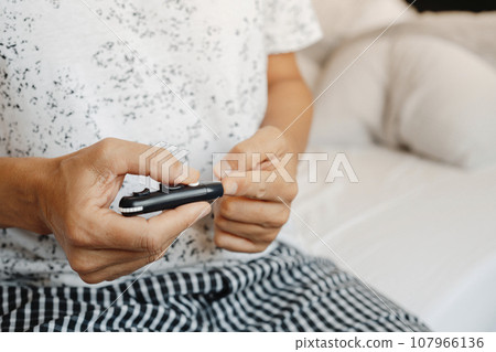 man in bed pricking his finger with a fingerstick 107966136