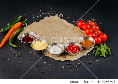 Set of different bowls of various dip sauces, on dark background served with vegetable Set of different bowls of various dip sauces, on dark background served with vegetable 107966701
