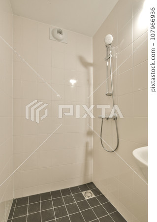 a white bathroom with black tile flooring and shower head mounted on the wall in front of the toilet bowl a white bathroom with black tile flooring and shower head mounted on the wall in front of the toilet bowl 107966936