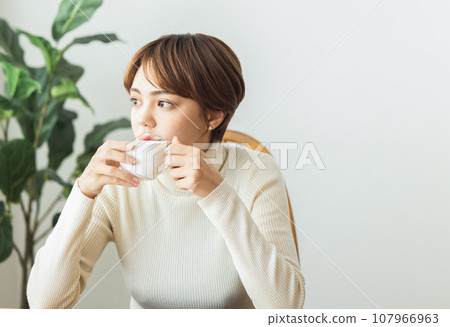 A woman who drinks coffee in a room 107966963