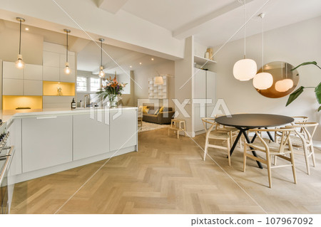 a kitchen and dining area in a modern apartment with white walls, wood flooring and light grey cabinetry a kitchen and dining area in a modern apartment with white walls, wood flooring and light grey cabinetry 107967092