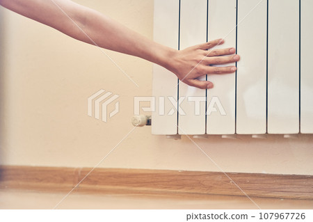 A woman's hands at the heating battery at home, after a walk in cold winter weather. A woman touches a barely warm battery during the heating season, or checks the heating system. High quality photo 107967726