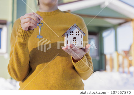 woman holds key and a model of mock-up of house in her hands. sale of real estate construction 107967870