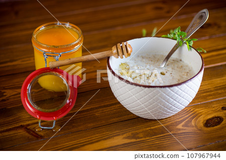 milk oatmeal porridge with honey for breakfast in a bowl wooden table. 107967944