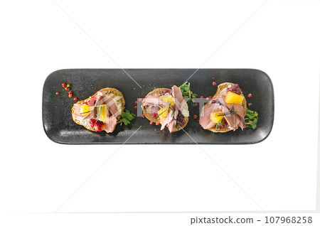 Bruschetta with duck, cowberry jam and orange on black ciabatta toast isolated 107968258