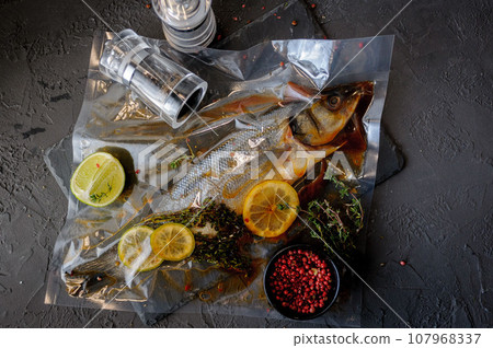 Raw sea bass fish with spices and herbs ingredients on black background Raw sea bass fish with spices and herbs ingredients on black background 107968337