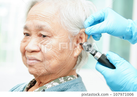 Otolaryngologist or ENT physician doctor examining senior patient ear with otoscope, hearing loss problem. Otolaryngologist or ENT physician doctor examining senior patient ear with otoscope, hearing loss problem. 107971006