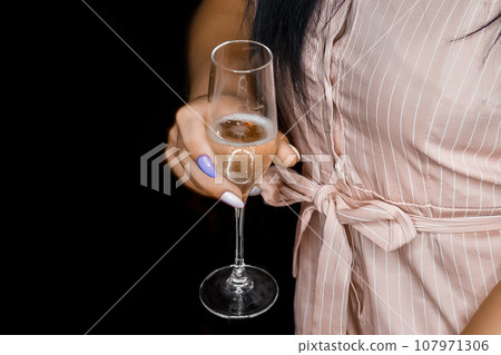 Hand of a young girl holding a glass of light alcohol, chilled champagne, close-up against the black background Hand of a young girl holding a glass of light alcohol, chilled champagne, close-up against the black background 107971306