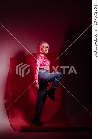 Woman model sitting on pink background at photo shoot in studio. 107972551