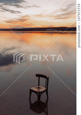 Sunset over a lake with an empty chair in the water Sunset over a lake with an empty chair in the water 107972559