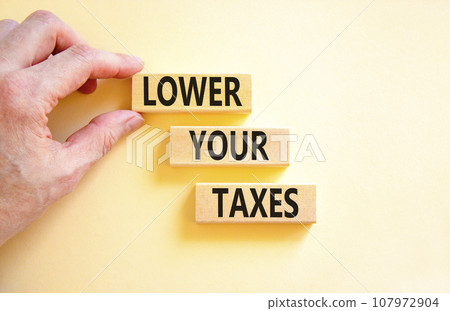 Lower your taxes symbol. Concept words Lower your taxes on wooden blocks on a beautiful white table white background. Businessman hand. Business tax lower your taxes concept. Copy space. Lower your taxes symbol. Concept words Lower your taxes on wooden blocks on a beautiful white table white background. Businessman hand. Business tax lower your taxes concept. Copy space. 107972904