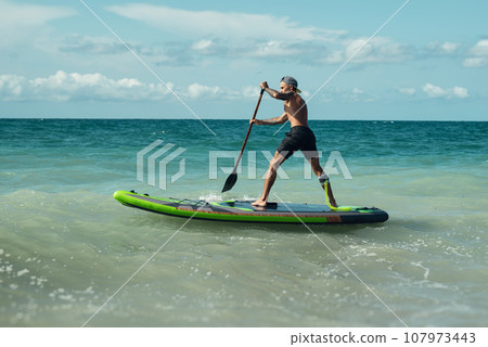 athletic wiry surfer guy swims with a paddle on a sup board in the sea athletic wiry surfer guy swims with a paddle on a sup board in the sea 107973443