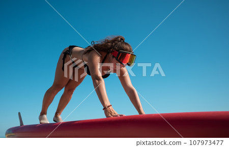 athletic girl in a swimsuit doing stretching on a sup-board in summer athletic girl in a swimsuit doing stretching on a sup-board in summer 107973477