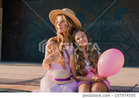 Portrait of mother and daughter in pink dresses with flowing long hair against the black backdrop. The woman hugs and presses the girl to her. 107974505