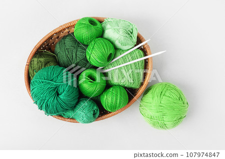 Green knitting balls in a basket with knitting needles on gray background. Set for the hobby of knitting warm clothes or toys. Concept needlework. Green knitting balls in a basket with knitting needles on gray background. Set for the hobby of knitting warm clothes or toys. Concept needlework. 107974847