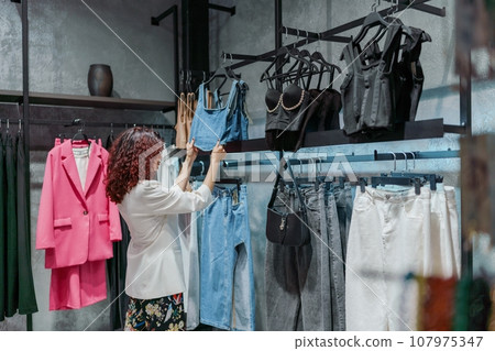 Shopping woman, women's fashion clothes in a store, boutique. Woman choosing clothes in a store 107975347