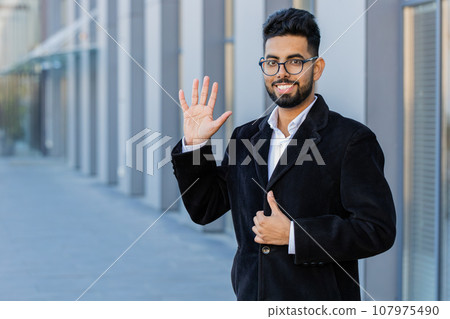 Business man smiling friendly at camera, waving hands hello, hi, greeting or goodbye in city street 107975490